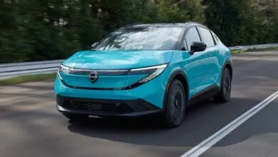 A vibrant teal Nissan LEAF electric vehicle drives down a road.