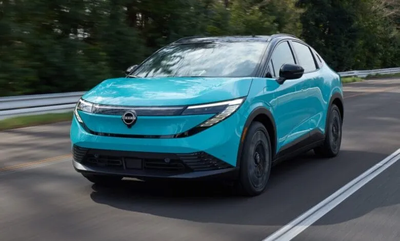 A vibrant teal Nissan LEAF electric vehicle drives down a road.
