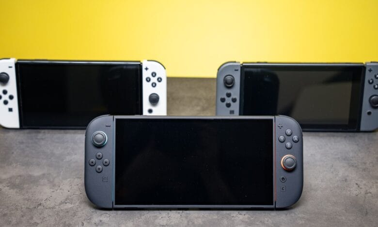 Three Nintendo Switch consoles in white, gray, and black, arranged on a gray surface against a yellow background. The screens are dark.