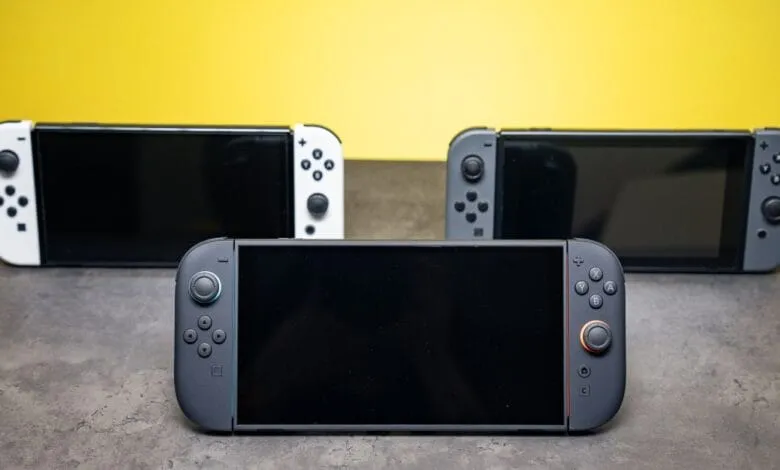 Three Nintendo Switch consoles in white, gray, and black, arranged on a gray surface against a yellow background. The screens are dark.