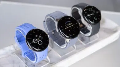 Three modern smartwatches displayed on stands, featuring blue, gray, and black bands.