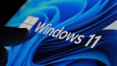 Close-up of a finger interacting with a Windows 11 screen displaying a blue, wave-like background.