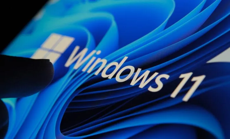 Close-up of a finger interacting with a Windows 11 screen displaying a blue, wave-like background.