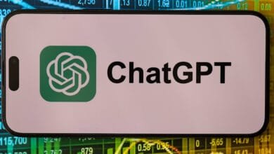 Close-up of a smartphone displaying the ChatGPT logo against a blurred background of stock market data.