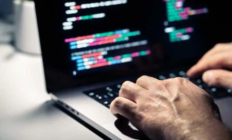 Close-up of hands typing code on a laptop at night. Lines of colorful code fill the screen.
