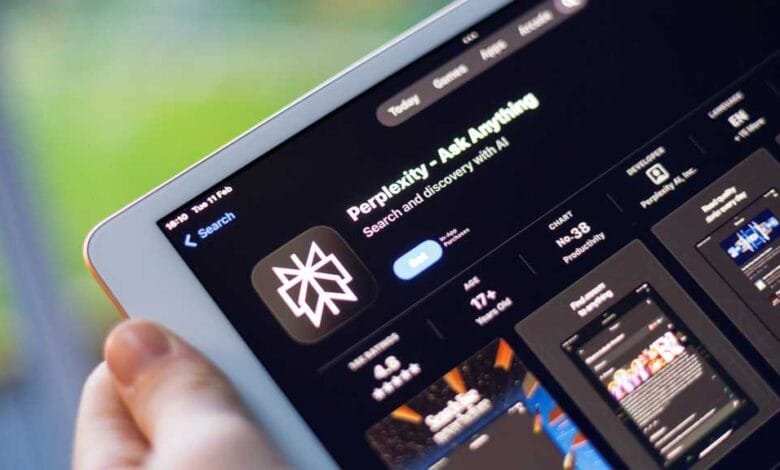 Close-up of a hand holding an iPad displaying the Perplexity AI app on the App Store. The app's icon and description are visible.
