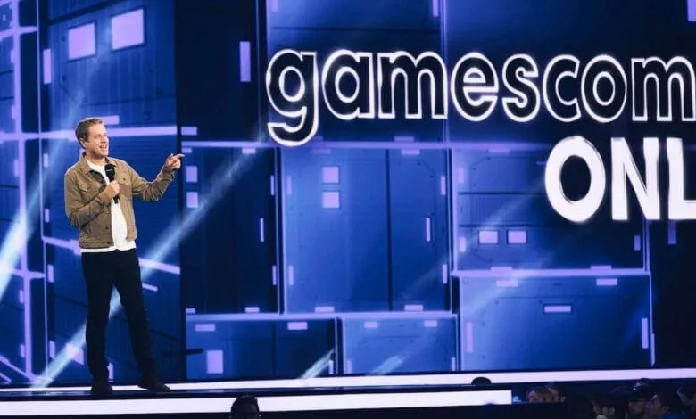 A man speaks at a Gamescom ONL event, gesturing with a microphone in hand against a blue digital backdrop.