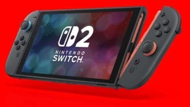 Nintendo Switch OLED model with coral Joy-Cons displayed against a red background. The console shows the Nintendo Switch logo and the number 2.