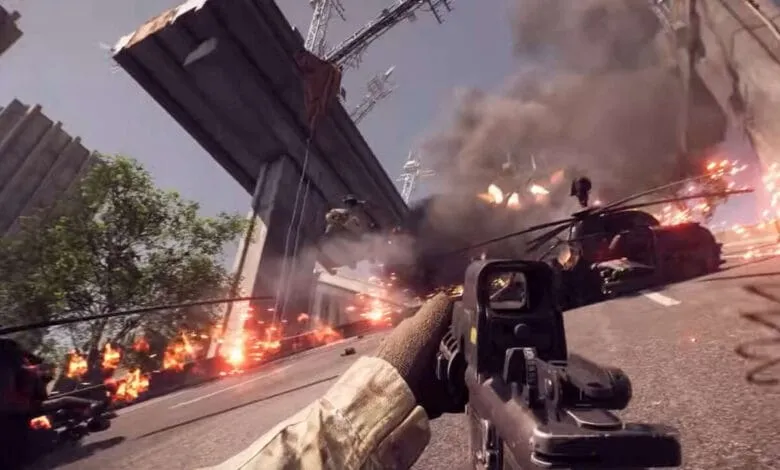 First-person view of a chaotic battlefield; explosions, burning vehicles, and a helicopter crash under a highway overpass.