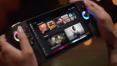 Person holding a handheld gaming device, showcasing a vibrant game menu with titles like Silksong and Gears. The device has illuminated controls.