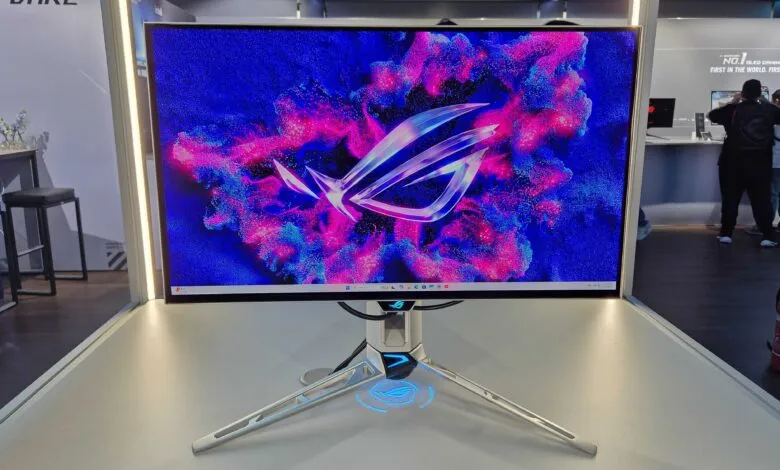 ASUS ROG OLED gaming monitor displayed on a stand with vibrant pink and blue abstract background.