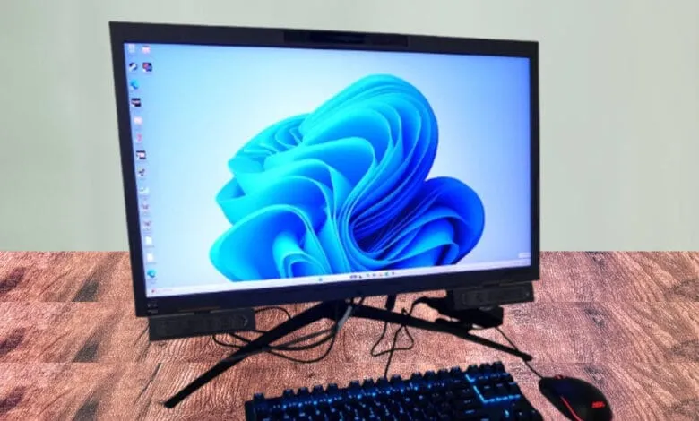 Modern computer setup with Windows 11 desktop visible, featuring a sleek monitor, keyboard, and mouse on a wooden desk.