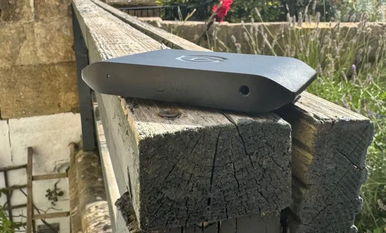 Black rectangular device rests on weathered wood, possibly a security camera or outdoor sensor.