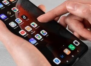 Close-up of hands using a smartphone displaying various app icons, including TikTok, Google apps, and others.