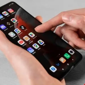 Close-up of hands using a smartphone displaying various app icons, including TikTok, Google apps, and others.