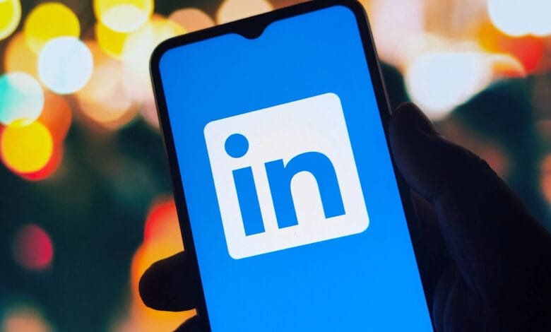 Close-up of a hand holding a smartphone displaying the LinkedIn app against a blurred city lights background.