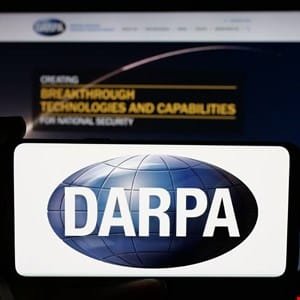 Close-up of a smartphone displaying the DARPA logo, with a DARPA website visible in the background.