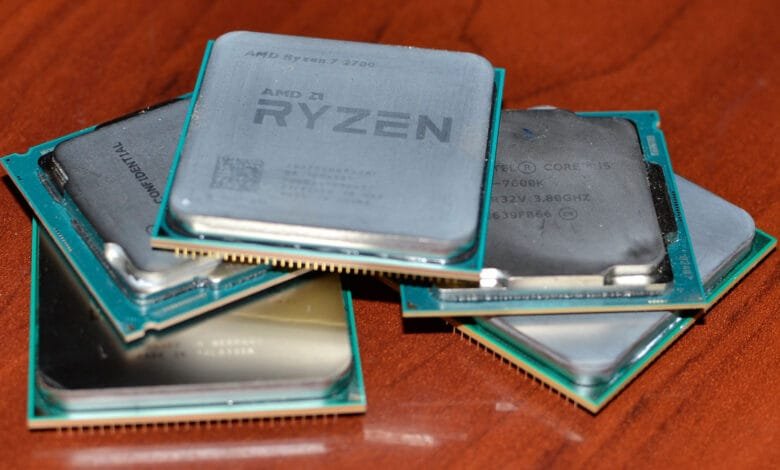 Close-up of several computer processors stacked on a wooden surface. Visible are AMD Ryzen and Intel Core i5 processors.