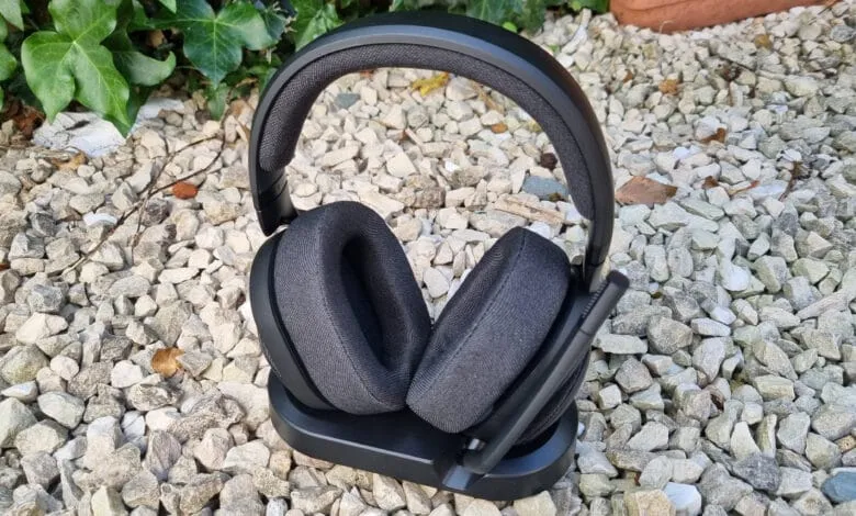 Black wireless gaming headset resting on its charging base, outdoors on gravel.