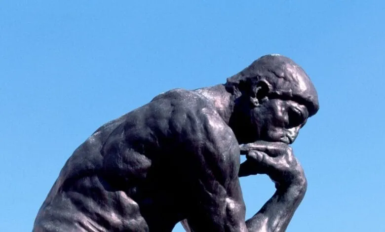 Close-up of Rodin's The Thinker statue, a bronze figure in deep thought against a clear blue sky.
