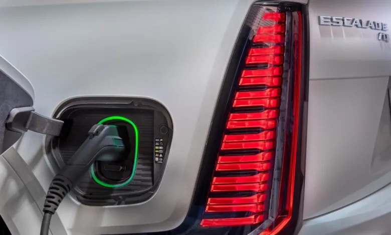 Close-up of a white Cadillac Escalade IQ charging port with a charging cable plugged in, and its distinctive rear taillight.