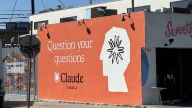 Large orange mural advertising Claude.AI with the tagline 'Question your questions' and a stylized head graphic.
