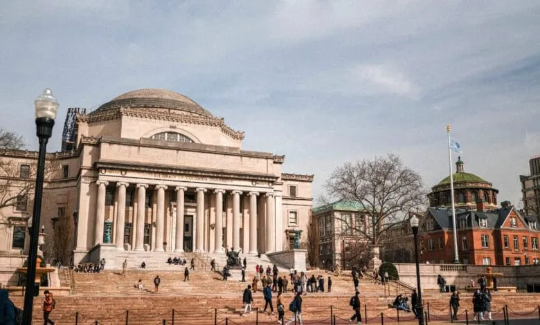 Columbia University's Low Memorial Library, a grand neoclassical building with a large staircase, surrounded by students on a sunny day.