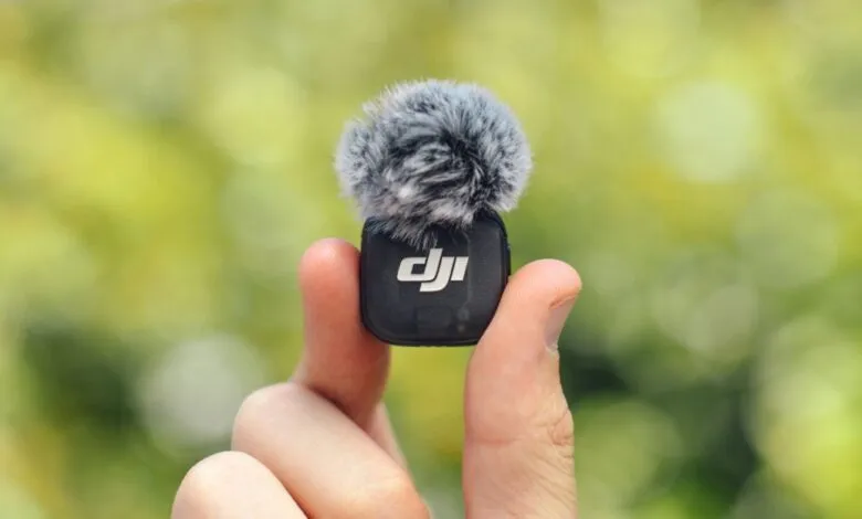 Close-up of a DJI wireless microphone with a furry windscreen held between fingers.