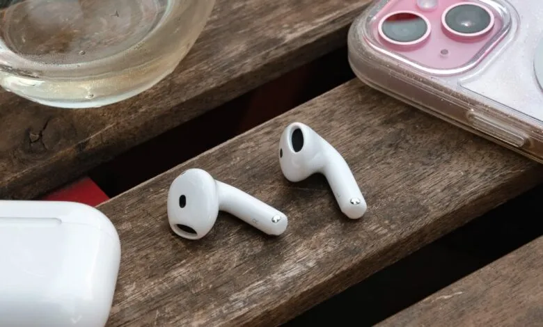 Pair of white Apple AirPods on wooden surface, next to phone and charging case.