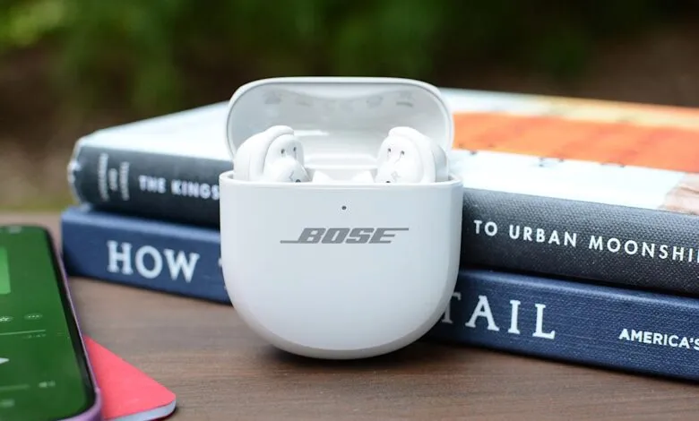 White Bose earbuds in their charging case, resting on a stack of books.