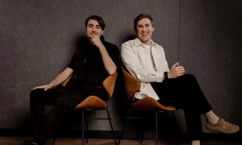 Two men, ElevenLabs co-founders, sit in tan chairs against a dark gray background. They smile at the camera.