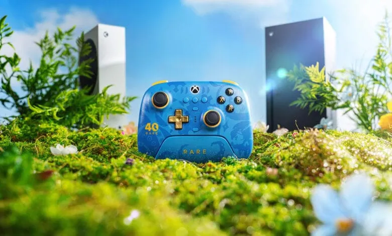 A vibrant blue Xbox controller with gold accents sits in a bed of moss, flanked by blurred Xbox Series X consoles. Celebrating 40 years of Rare.