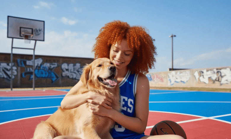 Woman with curly red hair hugs her Golden Retriever on a basketball court.