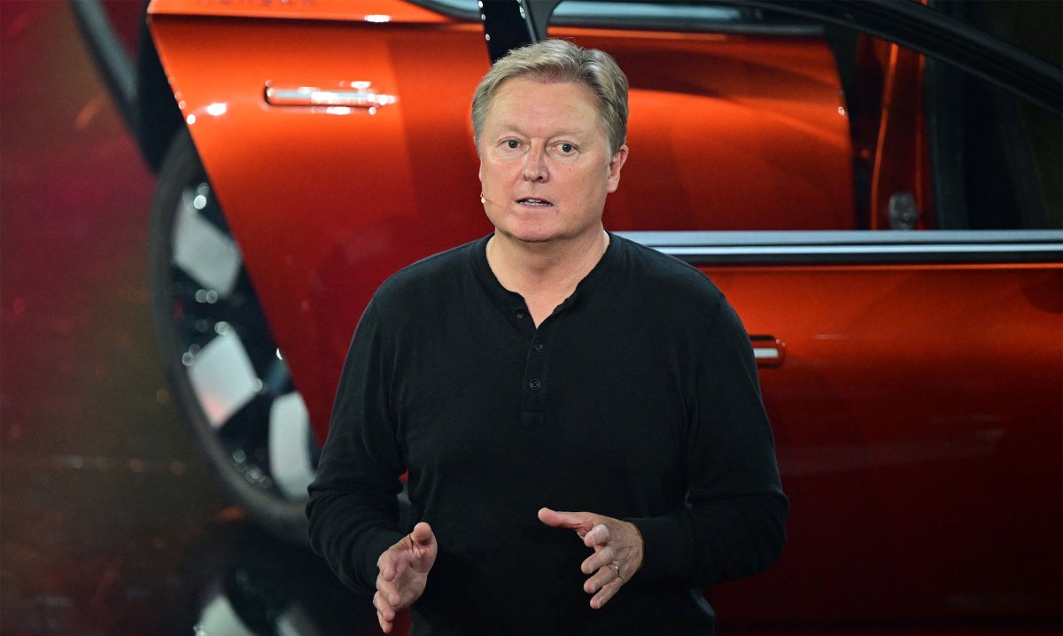 CEO speaking at a product launch event, standing in front of a vibrant red car.