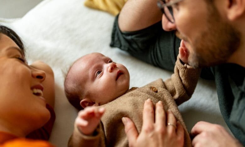 Happy parents lie on a bed with their newborn baby, gazing lovingly at their child.