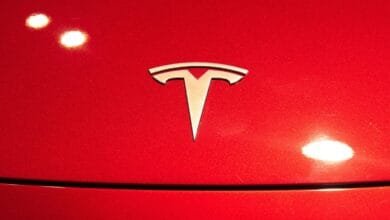 Close-up of a silver Tesla logo on a vibrant red car hood.