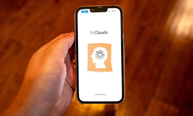 A hand holds a smartphone displaying the Claude AI app by Anthropic. The app's logo features a stylized head with a flower inside.