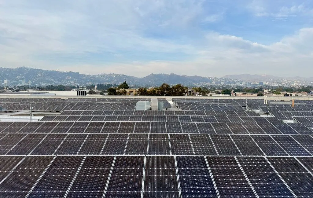 Vast array of solar panels on a rooftop, overlooking a cityscape and mountains.