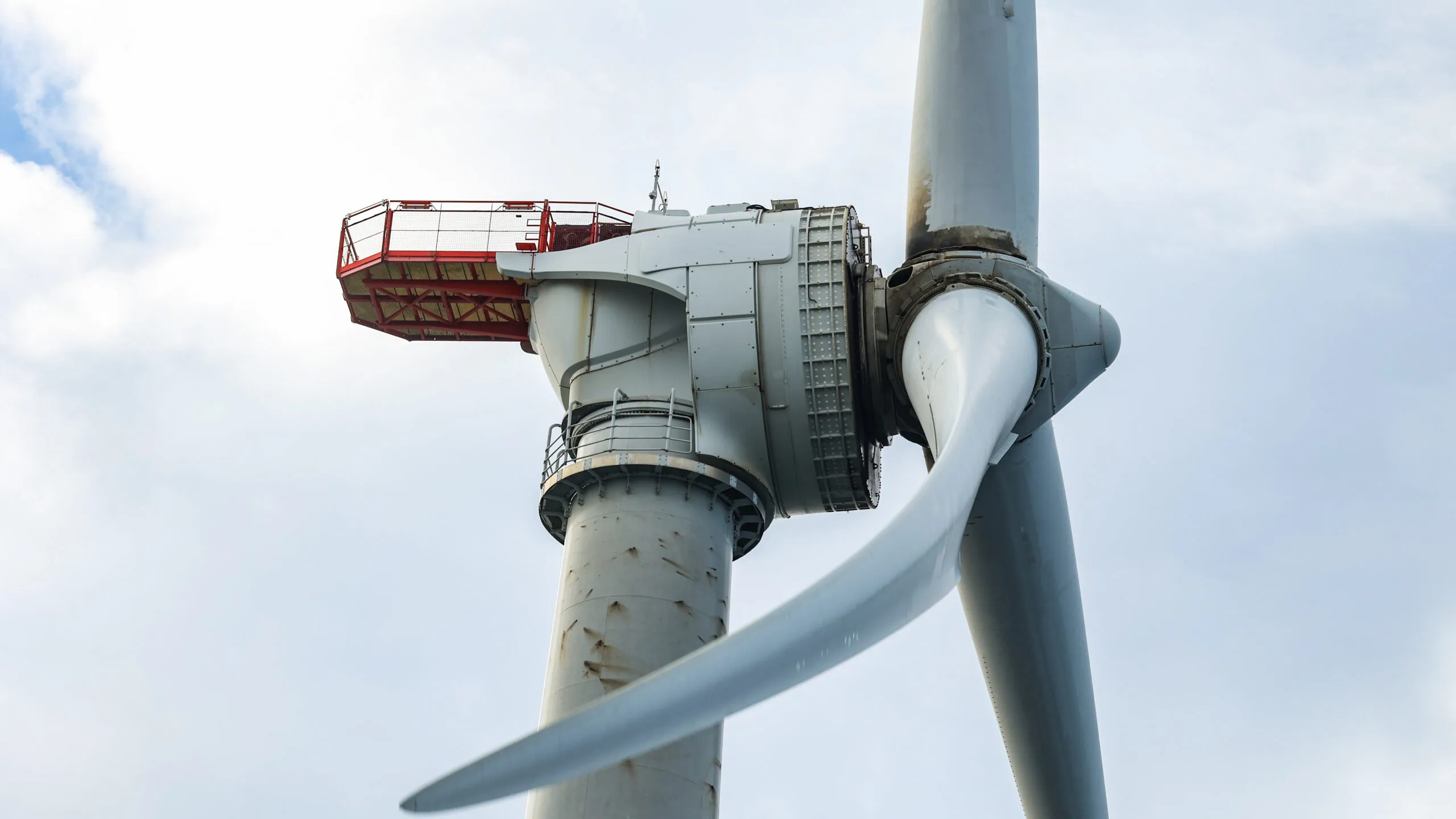 Close-up of a wind turbine's nacelle and blade, showing intricate details and a red access platform.