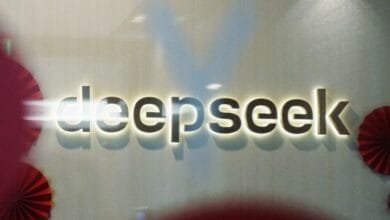 Close-up of the DeepSeek logo, illuminated and mounted on a light beige wall. Red paper decorations are visible in the corners.