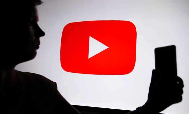 Silhouette of a person holding a phone up to a large screen displaying the YouTube logo.