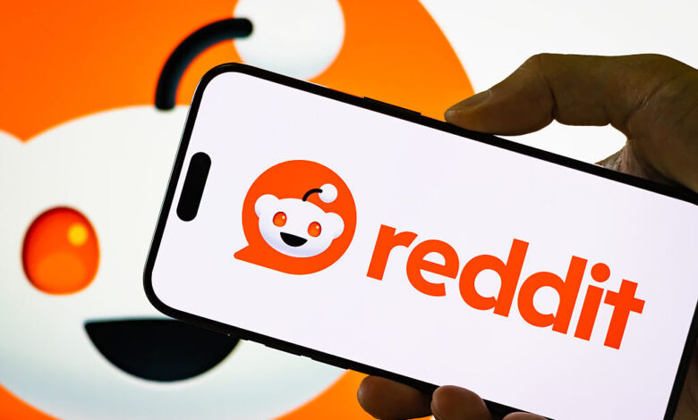 Close-up of a smartphone displaying the Reddit logo, with the Reddit mascot Snoo visible in the blurred background.