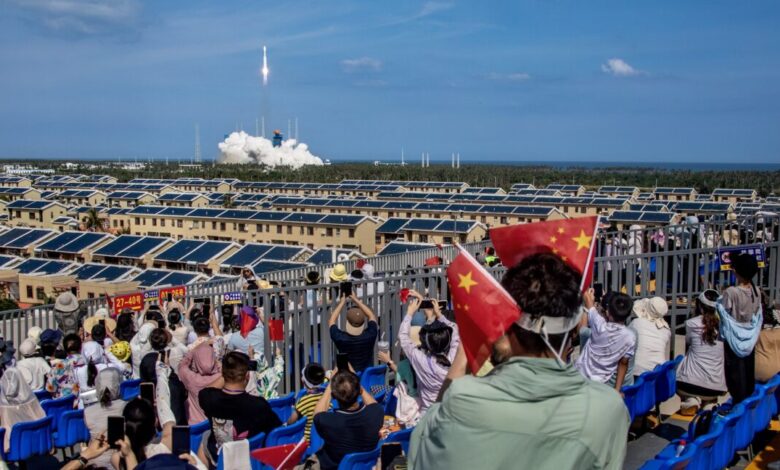 A Long March-8A rocket launches a group of low Earth orbit satellites in Wenchang, China, as spectators watch and wave Chinese flags.