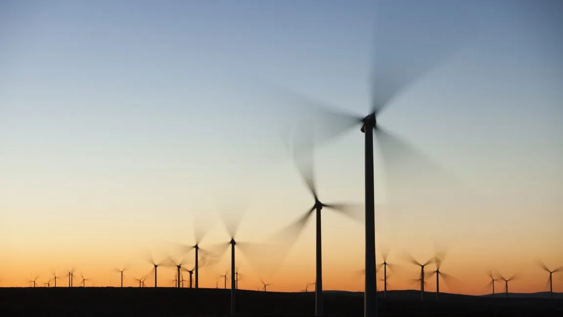 Wind turbines spinning at sunset, creating motion blur. Clean energy, renewable power.