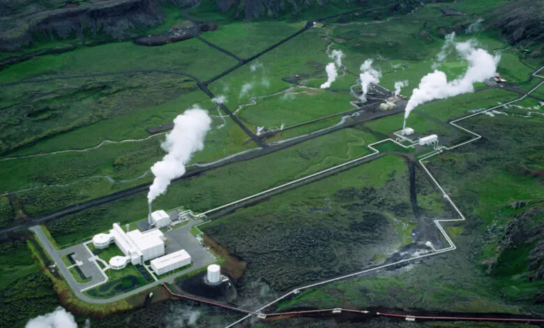 Aerial view of a geothermal power plant with steam rising in a lush green landscape.