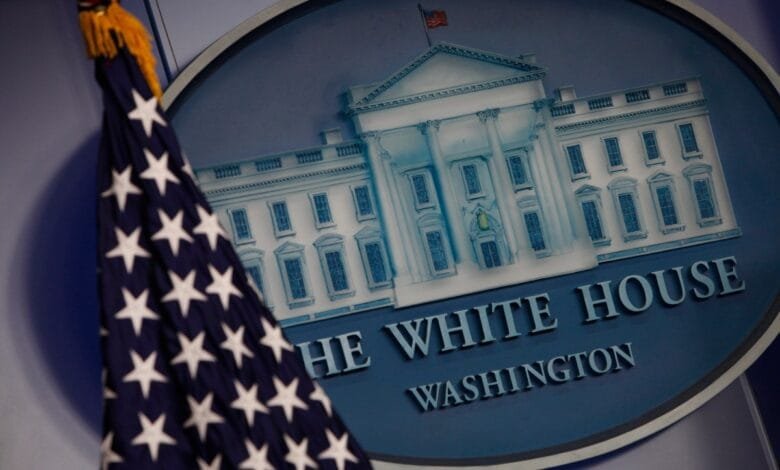 Close-up of the White House emblem with an American flag; depicts the White House building and text 'The White House Washington'.