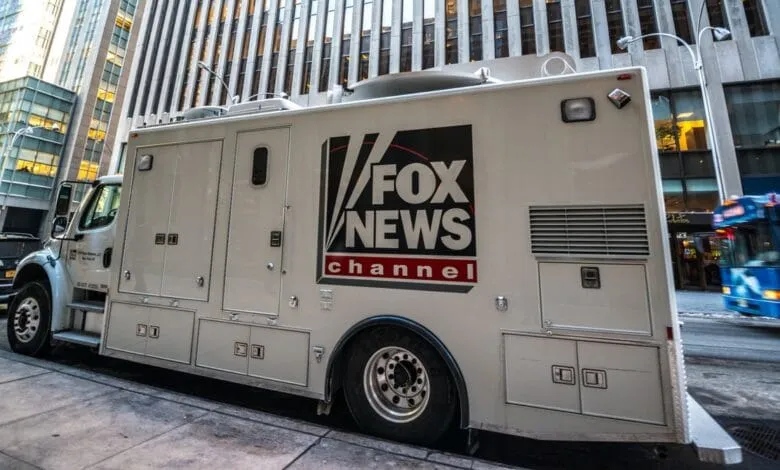 A Fox News Channel broadcast truck parked on a city street, next to tall buildings.