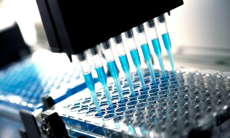 Close-up of a multichannel pipette dispensing a light blue liquid into a microplate.