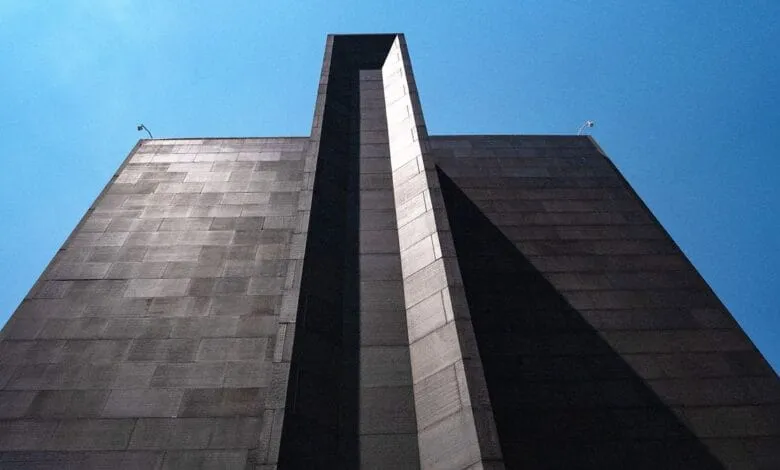 Low-angle view of a tall, gray stone building with a prominent vertical recess against a clear blue sky.