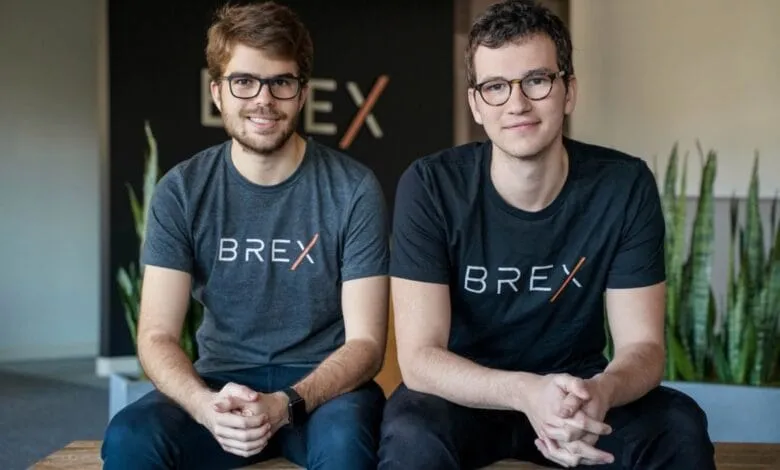 Two young men, wearing Brex-branded shirts, sit side-by-side and smile for a company portrait.